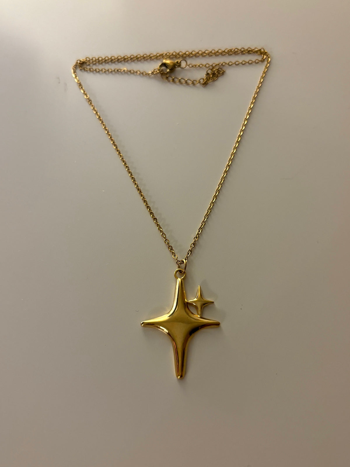Gold star-shaped pendant on a chain against a plain background