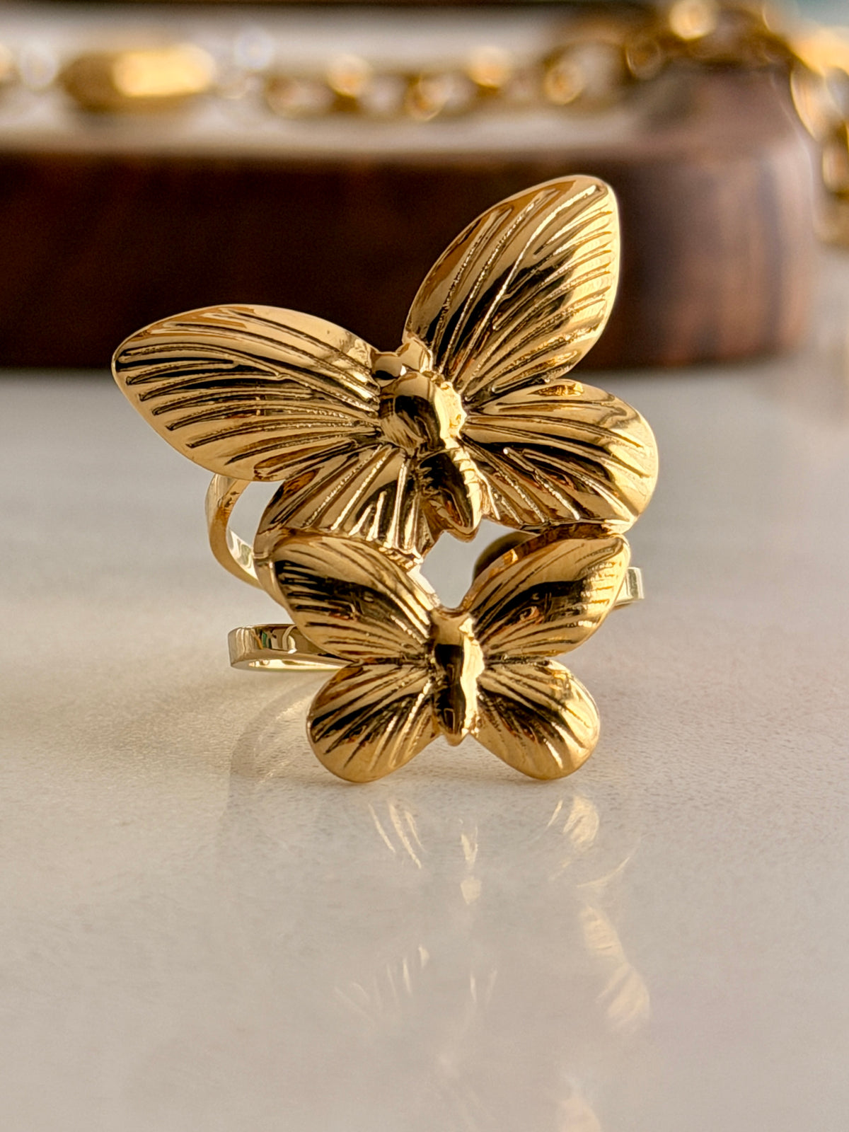 Gold butterfly ring on a reflective surface with a blurred background
