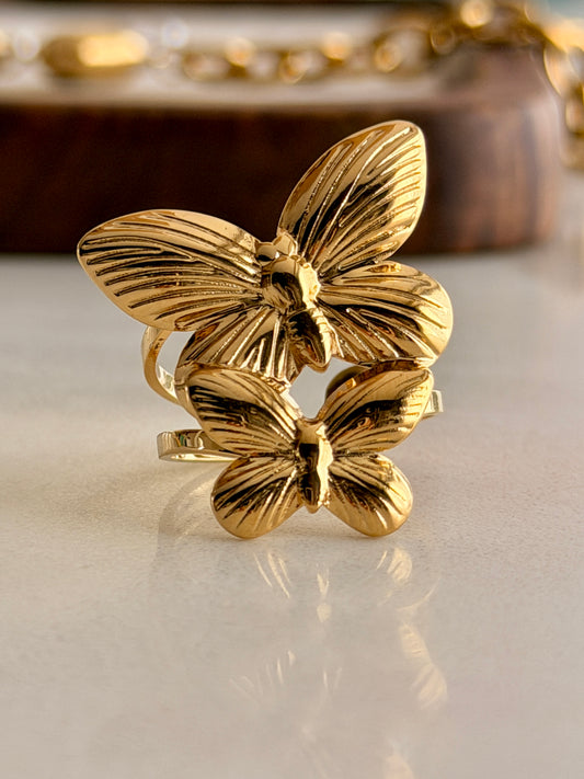 Gold butterfly ring on a reflective surface with a blurred background
