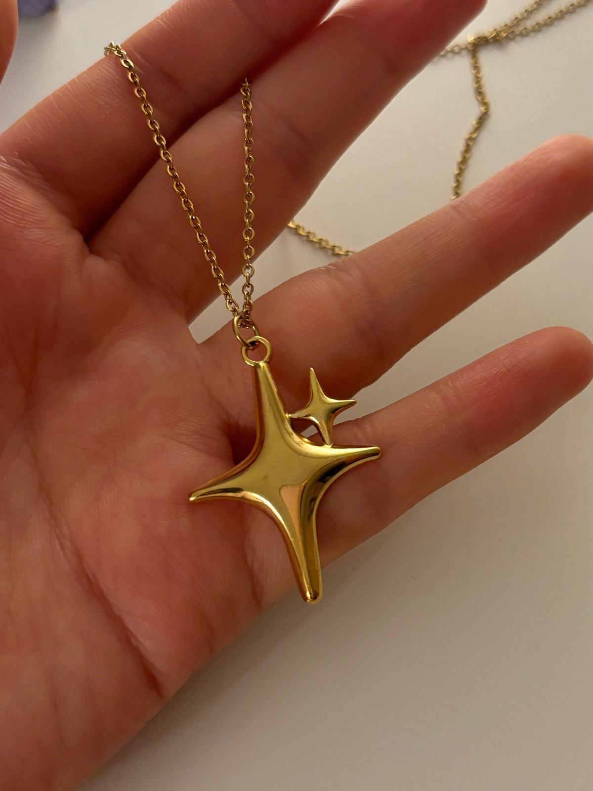 Gold necklace with a star-shaped pendant held in a hand against a neutral background