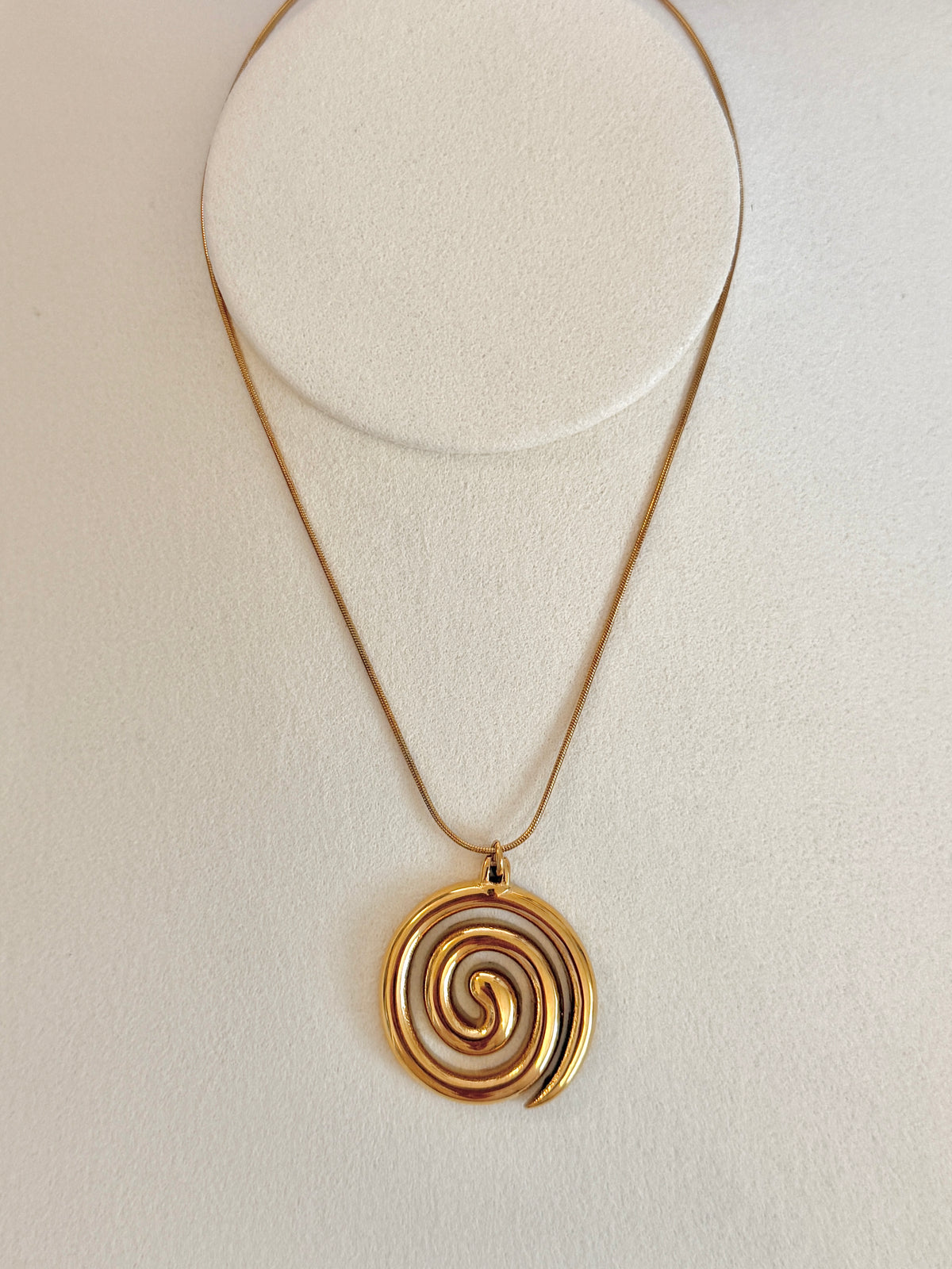 Gold spiral pendant necklace on a light beige background