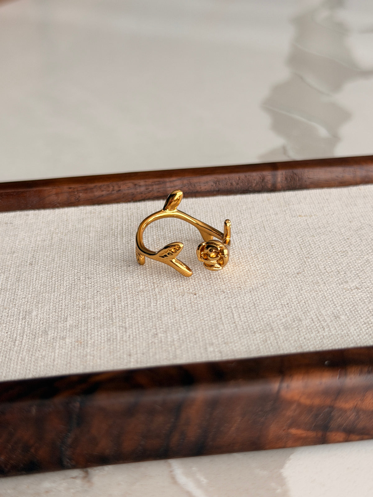 Gold rose-shaped ring on a textured white card with wooden sides.
