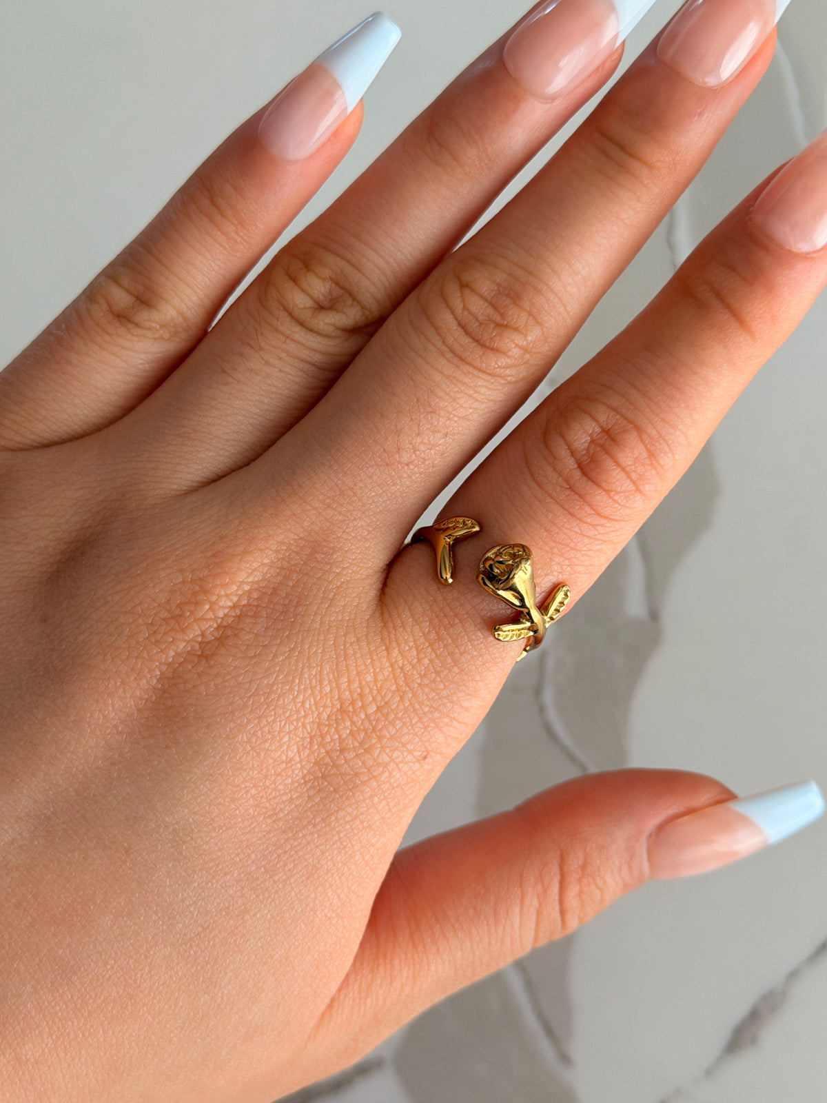 Gold rose ring on a person's finger with a neutral background