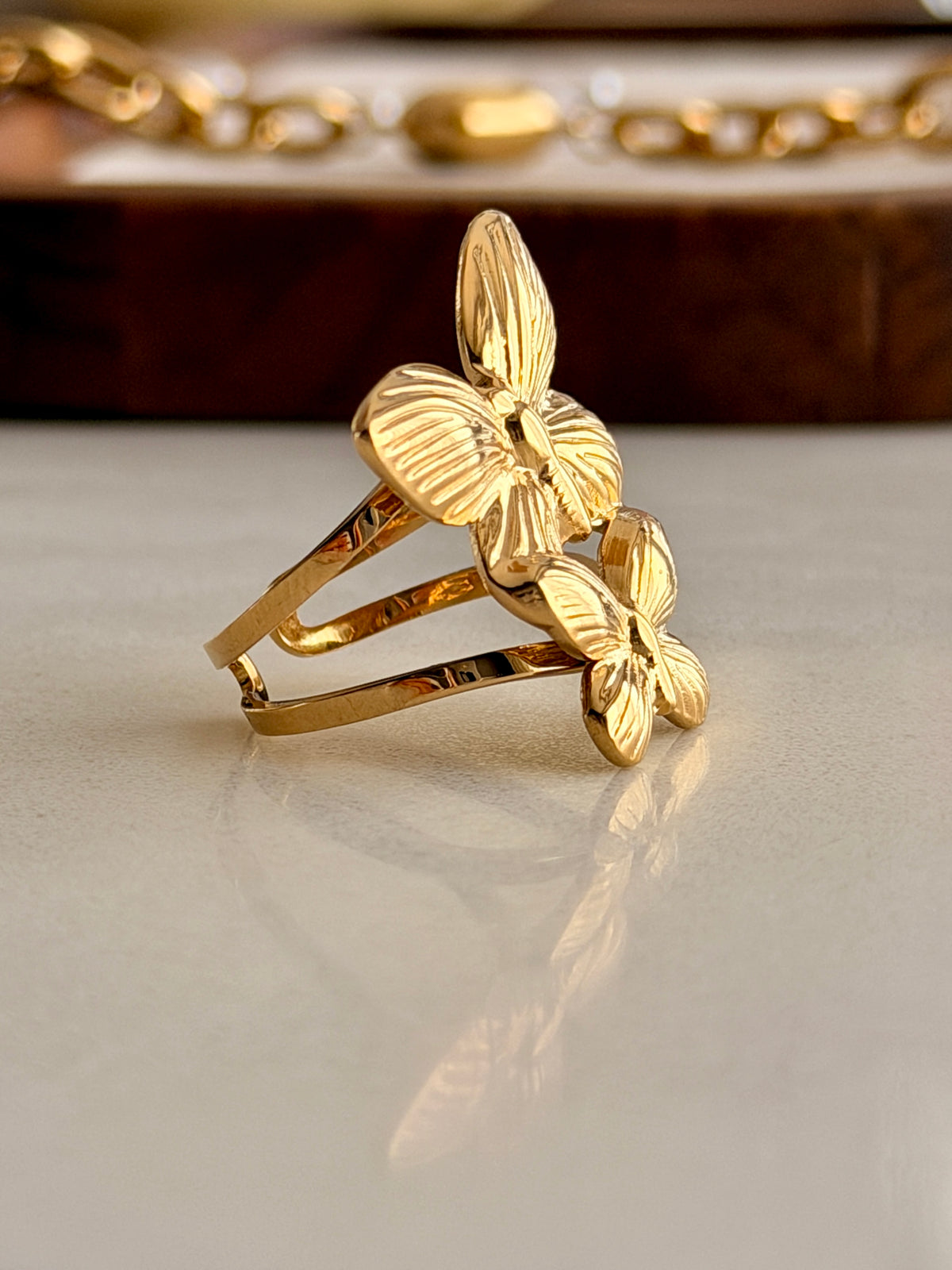 Gold butterfly ring on a reflective surface with a blurred background